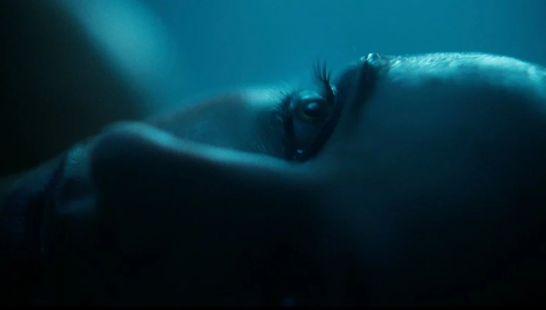 Close-up profile of a woman lying down under moody blue lighting, highlighting her eye and eyelashes.
