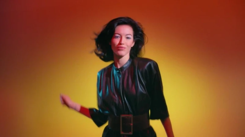 Stylish brunette woman in a black leather dress posing against a gradient orange and yellow backdrop in a studio setting.