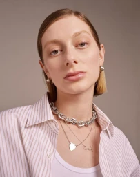 Portrait of a woman wearing layered silver necklaces, hoop earrings, and a striped shirt against a plain background