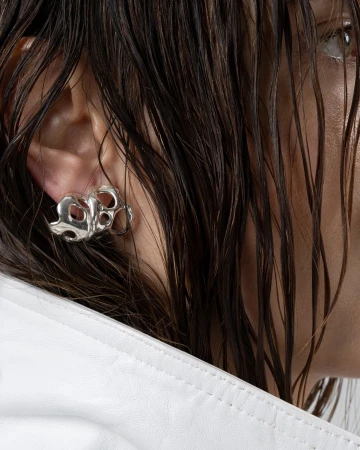 Close-up of a person with wet hair wearing a sculptural silver earring and white leather jacket, photographed by Clemence Demesme in Paris.