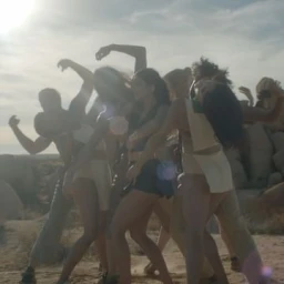 Group of dancers posing outdoors in a desert landscape under bright sun with lens flare effects