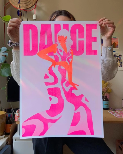Person holding a poster featuring a stylized female figure in a patterned dress with the word 'DANCE' in bold pink letters.