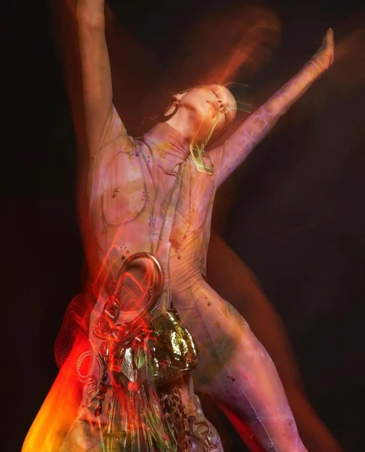 Artistic fashion shot of a woman in a body suit with accessories, arms raised, blurred motion effect against a dark background.