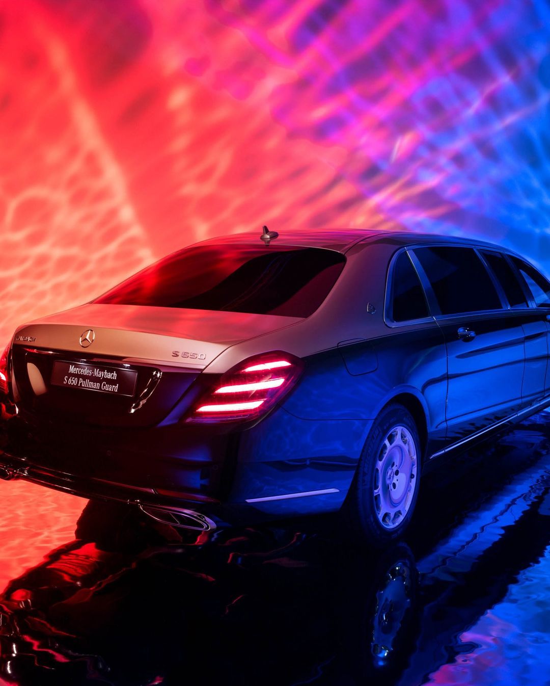 Luxury two-tone black and silver Mercedes-Maybach S 680 Pullman Guard sedan illuminated with blue and red lights on a wet surface.