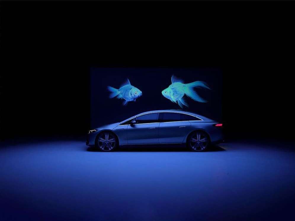 Sleek silver car showcased against a dark backdrop with ethereal blue fish illustrations floating above it in a captivating automotive display.