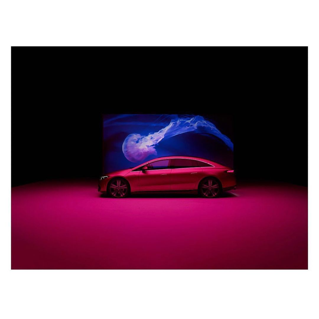 A modern red coupe is illuminated in a studio setting with a jellyfish graphic in the background, set against a black background.