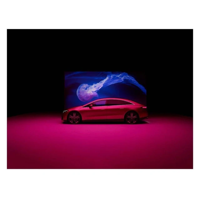 A modern red coupe is illuminated in a studio setting with a jellyfish graphic in the background, set against a black background.