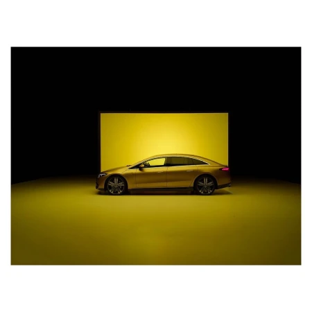 Sleek golden Mercedes-Benz EQS sedan car shown in a studio with a geometric yellow backdrop against a dark background.