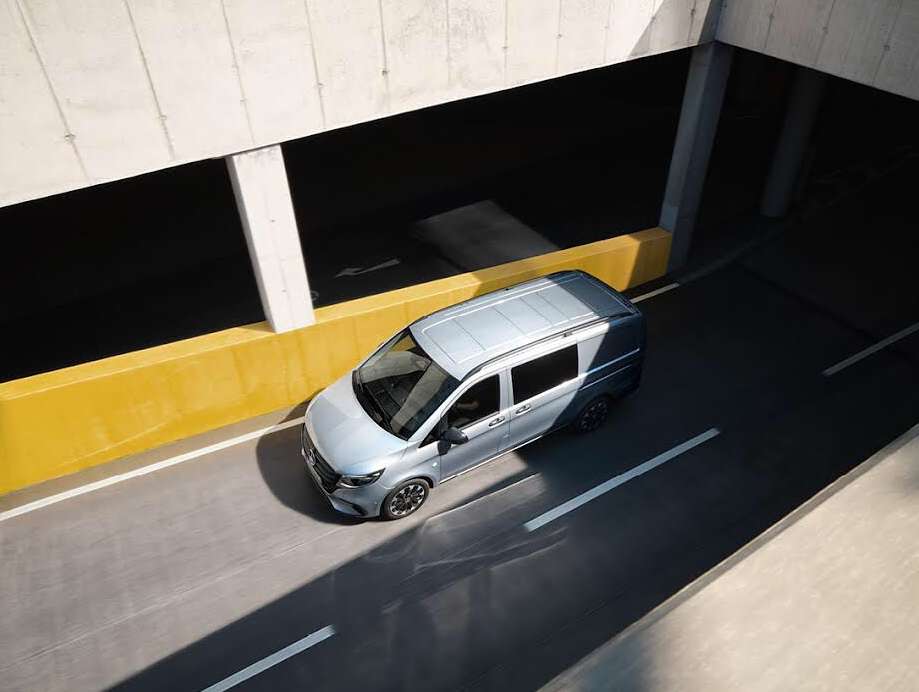 Aerial view of a light blue van on a concrete road, surrounded by architectural structures and bright yellow barriers. Automotive design.