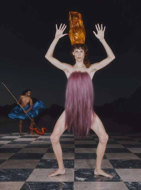Surreal portrait of a fair-skinned woman with a golden headpiece, standing on a checkered floor with a second figure in the background.