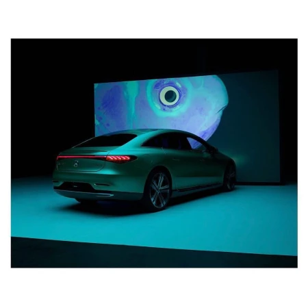 Sleek green Mercedes-Benz EQS coupe, rear view, in a dark studio setting with turquoise floor and abstract eye art projection backdrop.