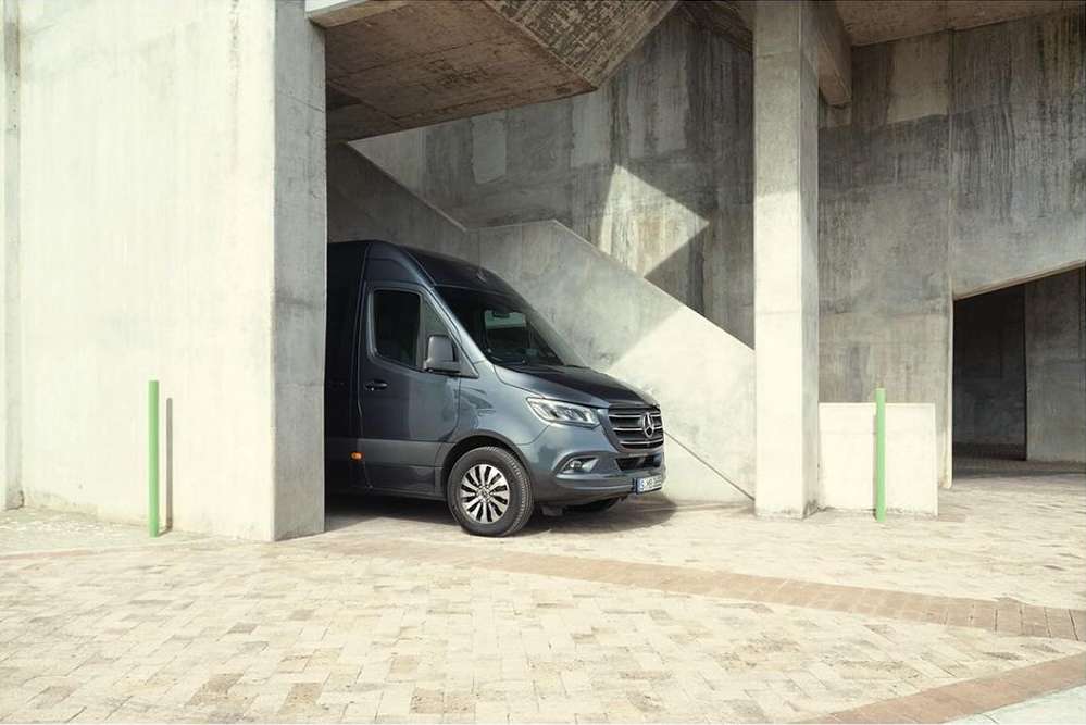 A grey Mercedes-Benz Sprinter van parked in an urban setting with concrete structures, good lighting, and visible tires.