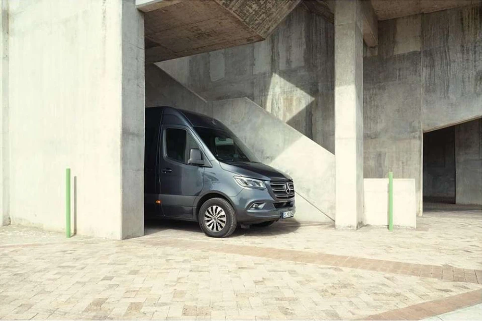 A grey Mercedes-Benz Sprinter van parked in an urban setting with concrete structures, good lighting, and visible tires.