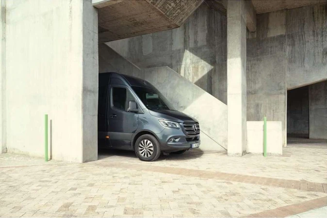 A grey Mercedes-Benz Sprinter van parked in an urban setting with concrete structures, good lighting, and visible tires.