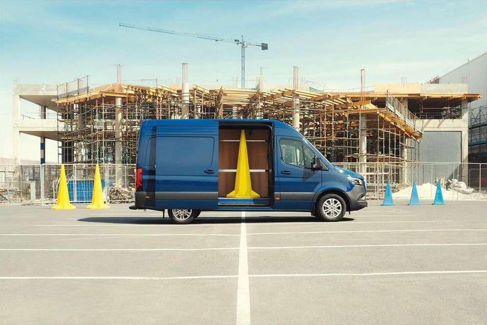 Blue van parked in a lot with construction cones and a building under construction in the background on a bright, sunny day.