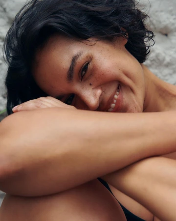 Close-up portrait of a smiling woman with short dark hair and freckles resting her chin on her crossed arms, photographed by Cleo Glover.
