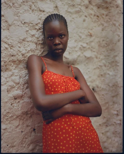 Woman in red polka dot dress poses against textured wall. Portrait of female with arms crossed, in natural light.