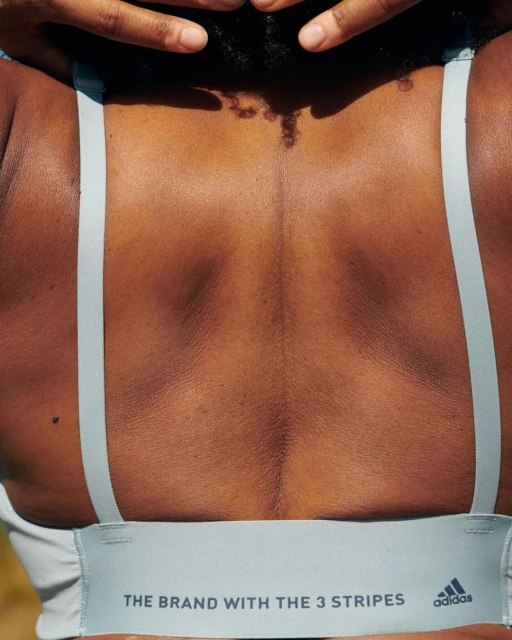 Woman's back wearing Adidas sports bra outdoors, showing athletic physique and the brand's three-stripe logo on the bra's band.