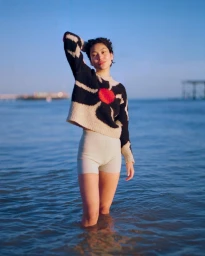 Woman standing in shallow ocean water wearing a black and white patterned sweater and white shorts, photographed by Cleo Glover.