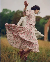 Woman in floral print midi dress dancing in a grassy field with trees in the background