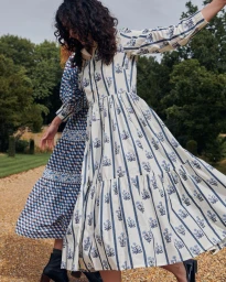 Two models in patterned dresses walking outdoors on a gravel path near a body of water captured by Cleo Glover.