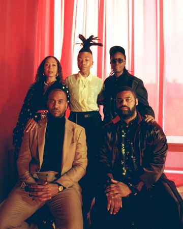 Portrait of five Black individuals posed together against a backdrop of vertical red curtains photographed by Clifford Prince King.