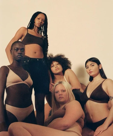 Group of five diverse female models posing together in underwear against a plain studio backdrop captured by Clifford Prince King