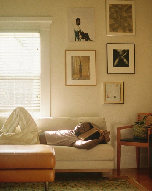 Man relaxes on a white sofa in a brightly lit living room with modern art hanging on the wall, creating a peaceful indoor scene.