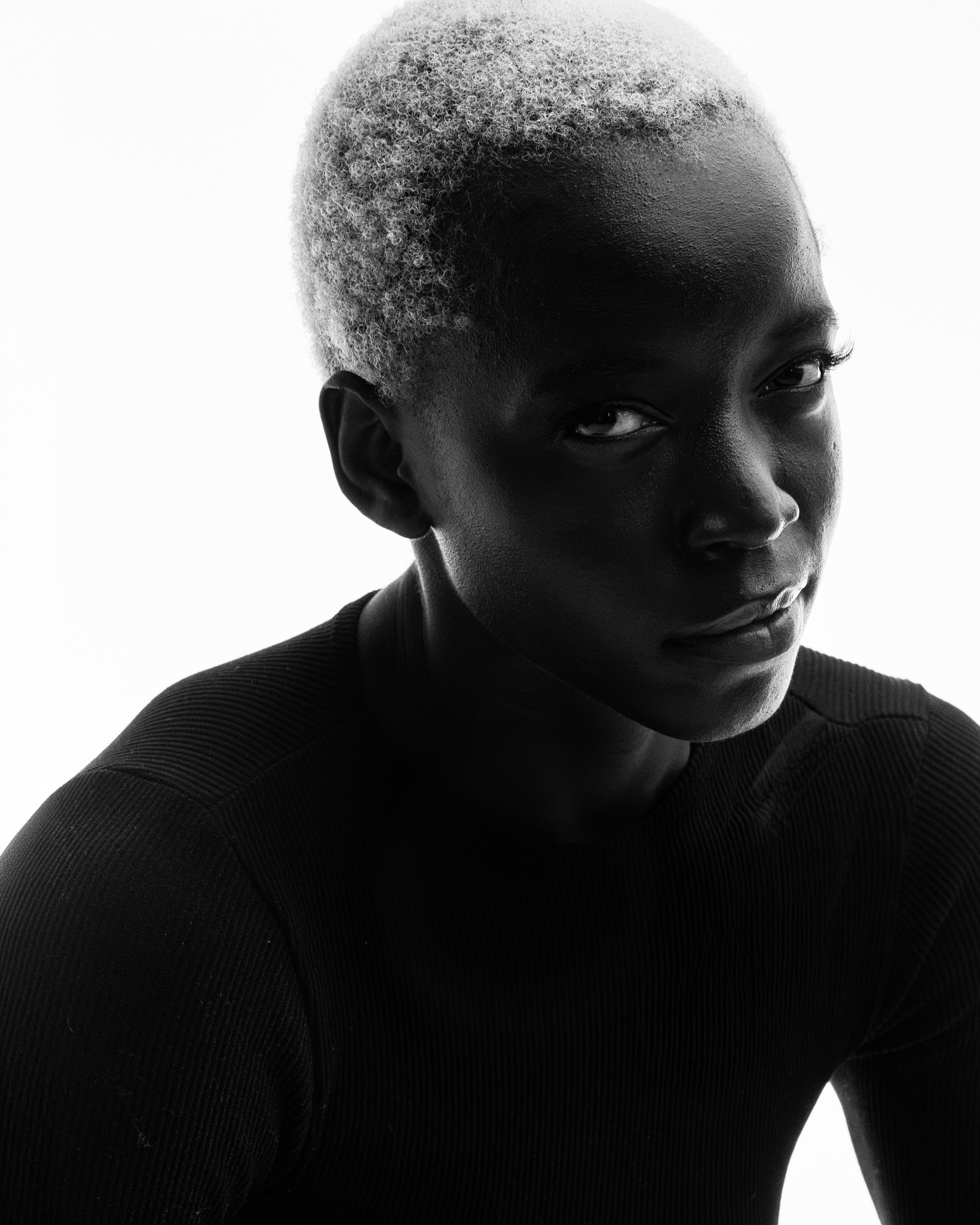 Portrait of an African American woman with short platinum blonde hair looking directly at the camera in a close-up black-and-white shot.
