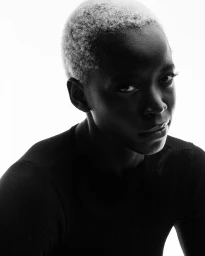 Portrait of a Black woman with short blonde hair wearing a black top against a bright white background