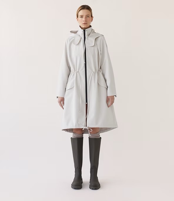 Full-length studio shot of a female adult wearing a grey hooded coat and dark grey knee-high boots against a neutral backdrop.