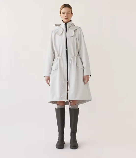 Full-length studio shot of a female adult wearing a grey hooded coat and dark grey knee-high boots against a neutral backdrop.