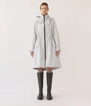 Full-length studio shot of a female adult wearing a grey hooded coat and dark grey knee-high boots against a neutral backdrop.