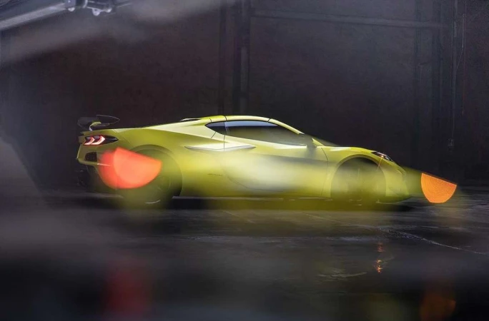 A yellow Chevrolet Corvette is in motion inside a dark studio, headlight beams extended for aerodynamic testing, captured with studio lighting.