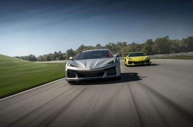 Silver sports car driving fast on a paved racetrack with a yellow sports car following behind under a clear blue sky