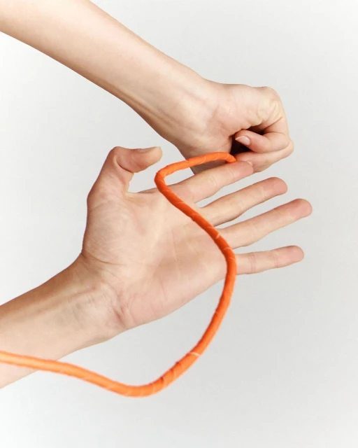 Close-up shot of two hands manipulating a length of orange rope against a plain white backdrop, showcasing dexterity and focus.
