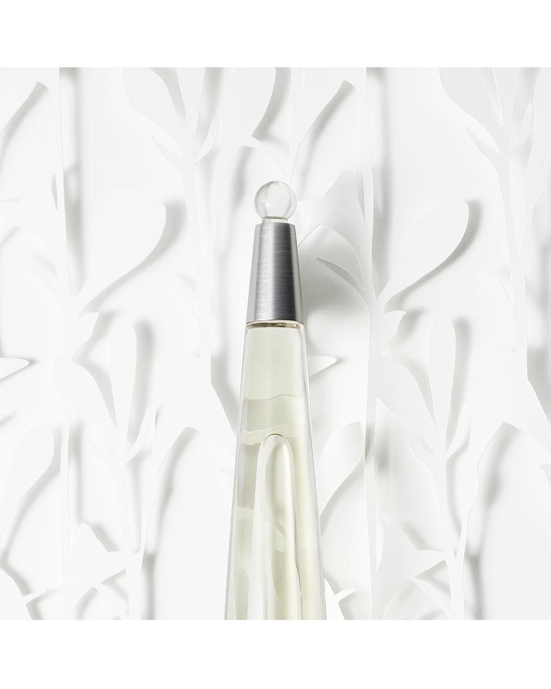 Elegant perfume bottle with a clear, sleek design against a textured white floral background, capturing a sense of minimalist beauty.
