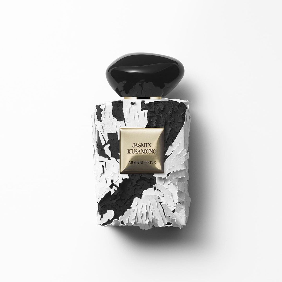 Close-up studio shot of a perfume bottle with a textured black and white design, and a glossy black cap against a white background.