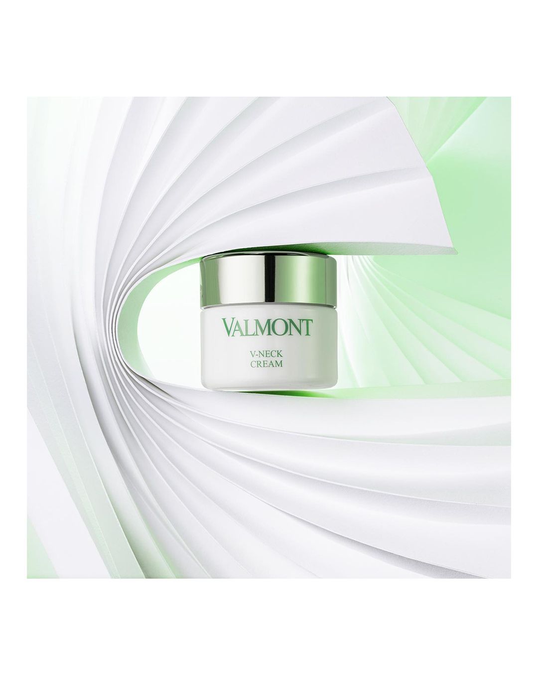 Cosmetic cream jar by Valmont with silver lid on white folded paper background, promoting beauty and skincare.