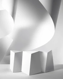 Monochrome architectural paper art sculpture with curved white paper sheets and geometric folded columns against a bright background.