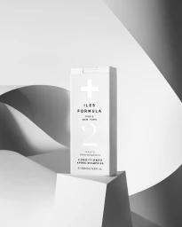 White Iles Formula conditioner bottle on a geometric white pedestal with curved paper backdrop