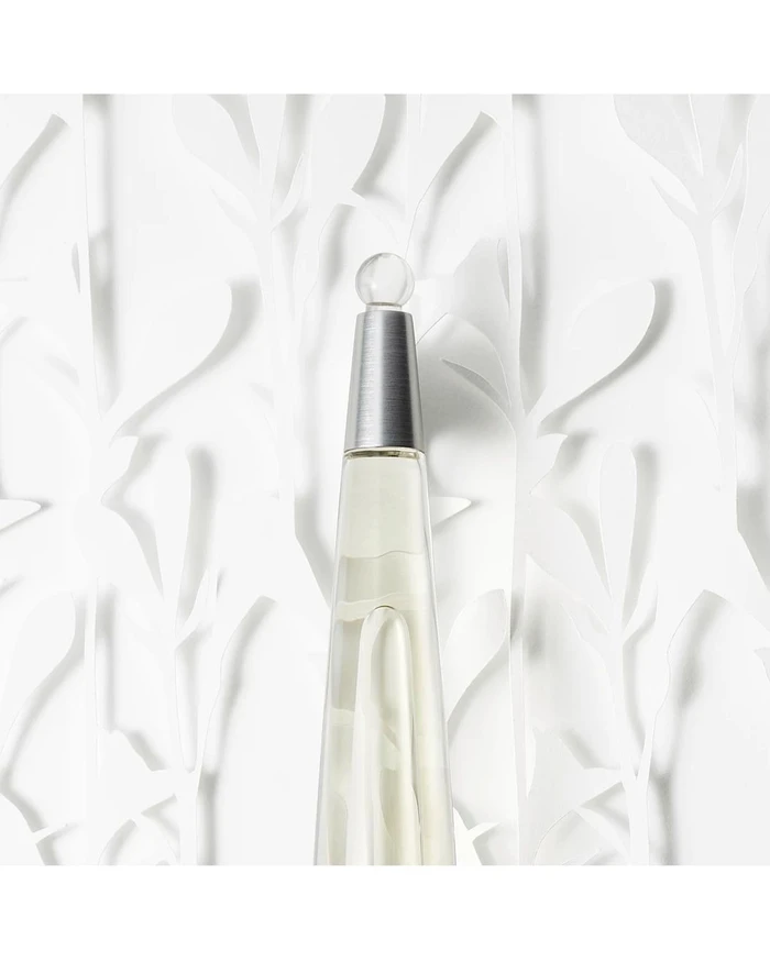 Close up of a tall conical perfume bottle with a metallic cap against a textured white paper art background.