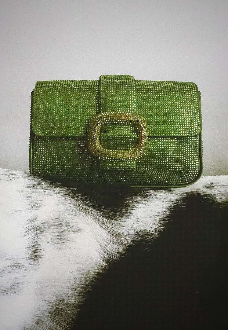 Close-up studio shot of a green clutch purse with a sparkling finish and gold clasp, placed on a black and white patterned surface.