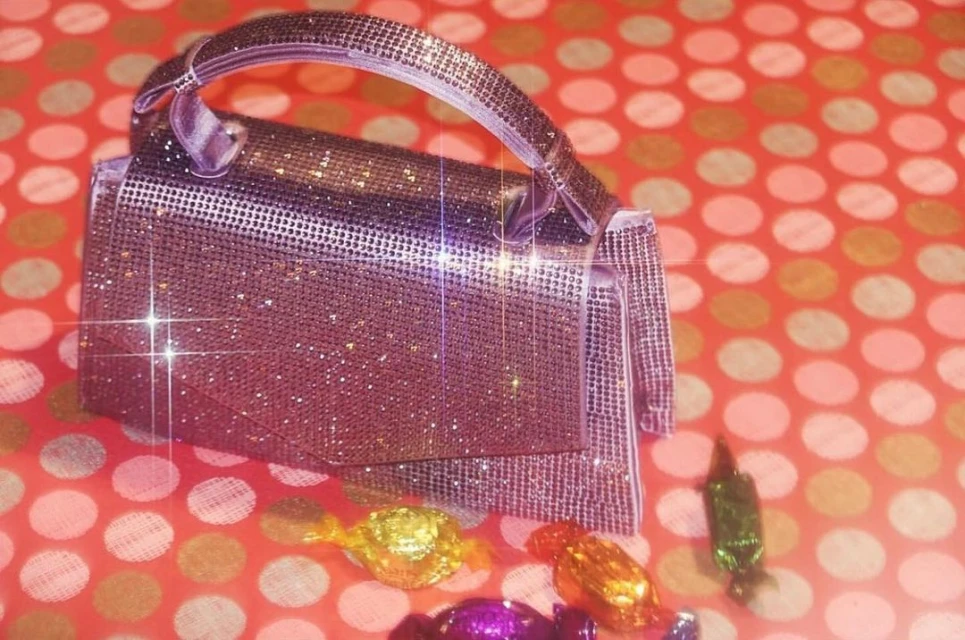 Shiny purple purse with handle and multi-colored wrapped candy pieces, placed on a red background with white polka dots.