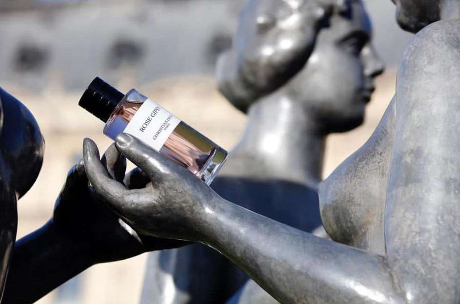 Perfume bottle held by statue in an outdoor setting, featuring the Christian Dior Rose Gypsy scent with a blurred background.