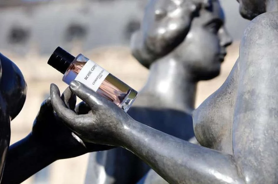 Perfume bottle held by statue in an outdoor setting, featuring the Christian Dior Rose Gypsy scent with a blurred background.