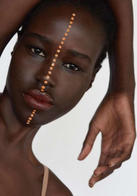 Portrait of a striking Black woman with artistic makeup. A line of orange dots extends from her forehead to her chin.