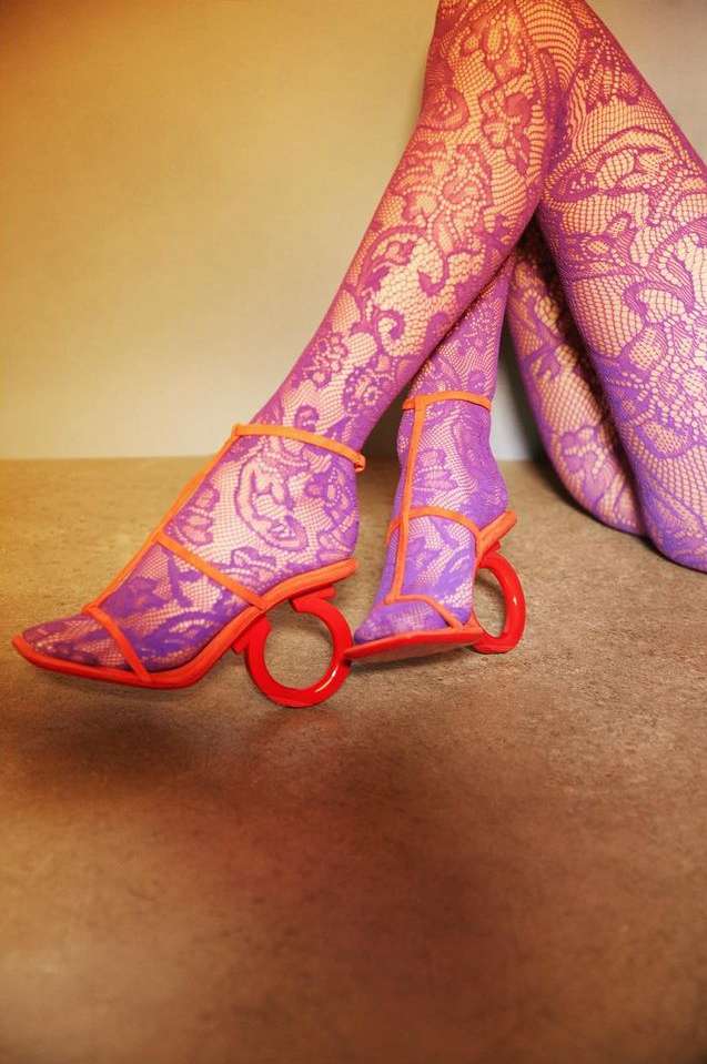 Close-up of unique red ring-heeled sandals with purple floral lace stockings, showcasing innovative fashion footwear design.