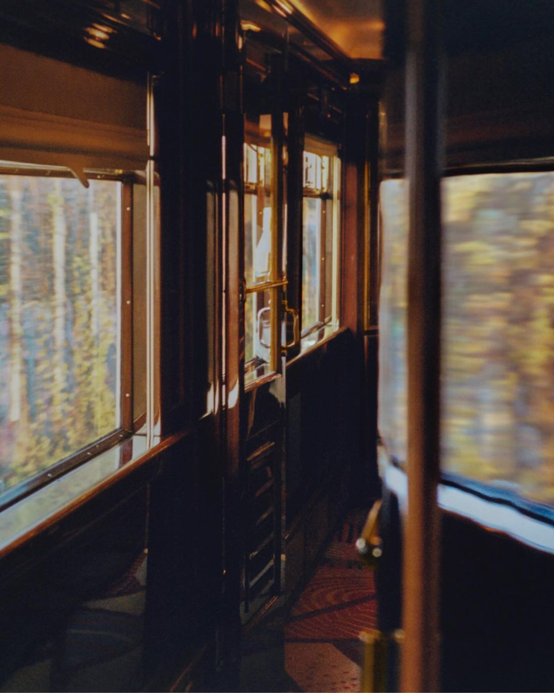 Interior view of a vintage train car with wood paneling, large windows, and sunlight streaming through, creating a warm and nostalgic atmosphere.