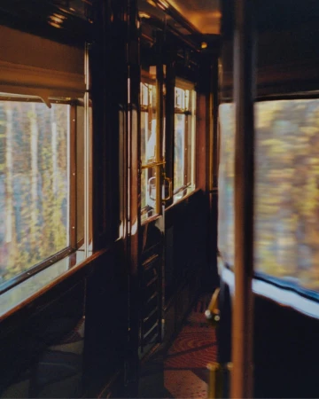 Interior view of a vintage train car with wood paneling, large windows, and sunlight streaming through, creating a warm and nostalgic atmosphere.